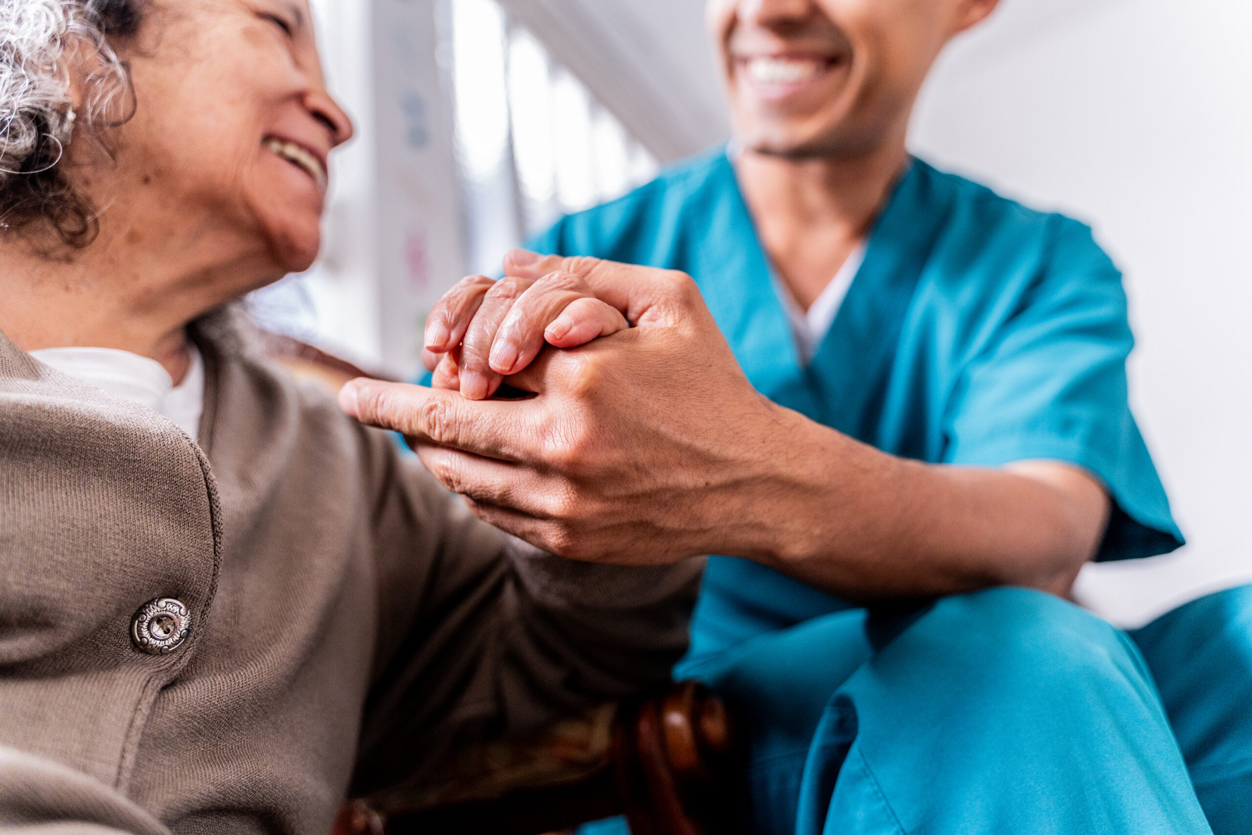 Senior woman holding caregiver's hands at home